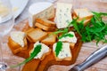 On table there is cutting board with blue cheese and hardtack decorated with arugula