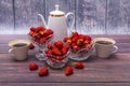 On wooden table are three vases filled with ripe strawberries, coffee pot and two mugs of coffee. Royalty Free Stock Photo