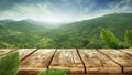 Wooden table top with green mountain background. Blue sky with sun light and green small leaves. Royalty Free Stock Photo