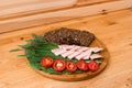 On the wooden table top is a round Board with sliced black bread with seeds, smoked brisket, tomatoes and herbs Royalty Free Stock Photo