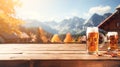 Wooden table top showcase with mug of beer on alpine village background, holiday flags, blank bokeh background