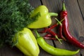 On a wooden table are two bell peppers, hot green peppers, hot red peppers and many small chillies with dill. Different types of Royalty Free Stock Photo