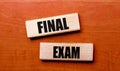 On a wooden table are two wooden blocks with the text FINAL EXAM