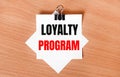 On a wooden table under a black paper clip lies a sheet of white paper with the text LOYALTY PROGRAM