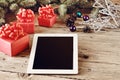 On the wooden table white tablet with Christmas presents closeup