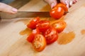 On a wooden table, a woman knifes a regimen of cherry tomatoes on slices for vegetable salad
