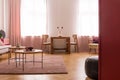 Wooden tables on purple carpet in living room interior with pink drapes at window. Real photo