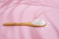 Wooden tea spoon filled with white rock salt, on pink background with palm leaf shadows Royalty Free Stock Photo