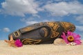 Wooden Tiki Mask on Sand With Flowers and Blue Sky Background