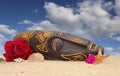 Wooden Tiki Mask on Sand With Flowers and Blue Sky Background