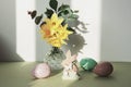 Wooden toy bunny and painted eggs, spring flowers on a green table against white wall with shadows. Easter concept Royalty Free Stock Photo