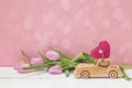 Wooden toy car carrying a heart and pink tulips on pink background. Royalty Free Stock Photo