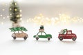 Wooden toy cars are carrying New Year's gifts and a Christmas tree on the roof. A Christmas tree and bokeh lights in the