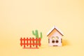 Wooden toy house from the constructor for children, brown fence and green cactus toy on a yellow background copy space