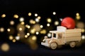 Wooden toy truck transporting Christmas ball on dark defocused lights background