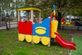 A wooden train of bright red, blue and yellow colors against a background of green trees and residential buildings Royalty Free Stock Photo