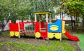 A wooden train of bright red, blue and yellow colors against a background of green trees and residential buildings Royalty Free Stock Photo