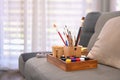 Wooden tray with paint brushes, tubes of paint couch in cozy home. Painters room with tools and supplies