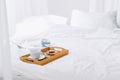 Wooden tray with seashells and tea set on white bed in modern bedroom. Royalty Free Stock Photo