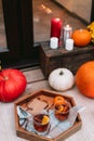 Wooden tray with spiced tea on the porch of the house decorated with pumpkins, flowers, and candles. Cozy home entrance