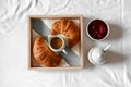 Wooden tray with tasty breakfast and with croissant, jam and coffee in bed on white bed linen. Top view Royalty Free Stock Photo