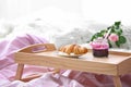 Wooden tray with tasty croissant, cup of coffee and jam on bed Royalty Free Stock Photo