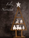 WOODEN TREE WITH CHRISTMAS FIGURES ON A STONE BACKGROUND WITH THE WORDS MERRY CHRISTMAS IN SPANISH