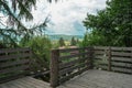 Wooden Viewpoint tower facing towards mountains covered with forests and an occluded village with cloudy skies