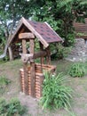 A wooden village well, made of cylindrical logs with a flexible tile roof, a wooden wheel and old rusty chain. Country style