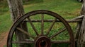 a wooden wagon wheel standing on grass near a fenced in field