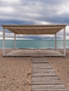 Wooden walkway and sunshades on sand beach with azure sea, cloudy sky background. Empty beach with sunshades. Evpatoriya, Crimea. Royalty Free Stock Photo