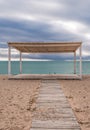 Wooden walkway and sunshades on sand beach with azure sea, cloudy sky background. Empty beach with sunshades. Evpatoriya, Crimea. Royalty Free Stock Photo