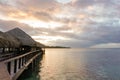 A wooden walkway with thatched roof bungalows leads out into the lagoon on the island of Moorea in French Polynesia at sunset; Royalty Free Stock Photo