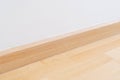 Wooden wall base skirting, finishing material with wood laminate floor and white mortar wall. Empty room with white wall and Royalty Free Stock Photo