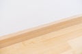 Wooden wall base skirting, finishing material with wood laminate floor and white mortar wall. Empty room with white wall and Royalty Free Stock Photo