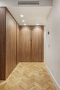 Wooden wardrobe with smooth doors in a room with herringbone oak flooring, spotlights in the false ceiling and ducted air