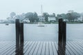 Wooden warf on grey rainy day looking out over estuary with boats anchored at beautiful houses on opposite shore Royalty Free Stock Photo