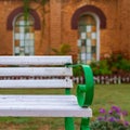 Wooden white garden bench with blurred background of orange wall with two huge windows in a public park Royalty Free Stock Photo