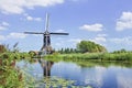 Wooden windmill mirrored in a canal on a summer day with a blue sky and clouds, Netherlands