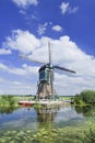 Wooden windmill near a canal on a summer day with blue sky and clouds, Netherlands.