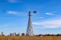 Wooden windmill pumps water into tough for cows out in winter pasture under blue sky with wispy clouds and behind rustic barbed wi Royalty Free Stock Photo