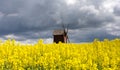 very old wooden windmill in rapseed field and sand road with dramatic storm clouds in background Royalty Free Stock Photo