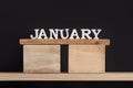 Wooden winter calendar months - January. Wooden letters and stand on black background