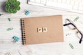 Wooden word PR in workspace on paper notepad with computer keyboard, glasses, supplies and green plant on light wood background