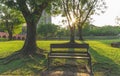 A wooden and wrought iron bench on fresh green carpet grass yard, smooth lawn under green trees beside a lake and brown bridge Royalty Free Stock Photo