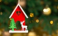 Wooden Xmas toy. House with deer. Christmas green tree with decorative items for winter season. Holidays background. Red and Royalty Free Stock Photo