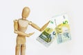 A wooden yellow mannequin holds Euro banknotes