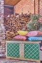 Woodpile of firewood, vintage chest and several colored pillows.