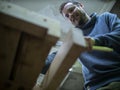 Woodworker with a beard sawing a wooden beam with a hand saw. a carpenter sawing a piece of wood.bottom view Royalty Free Stock Photo