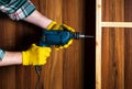 Woodworker drills a hole with an electric drill in a wood board. Close up of a foreman hand at work. Working environment in a